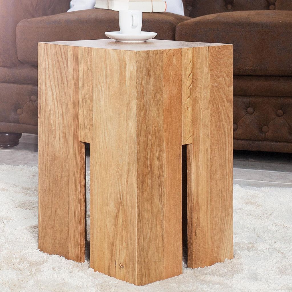 A wooden side table with a cup and saucer on top, placed on a rug next to a brown sofa.