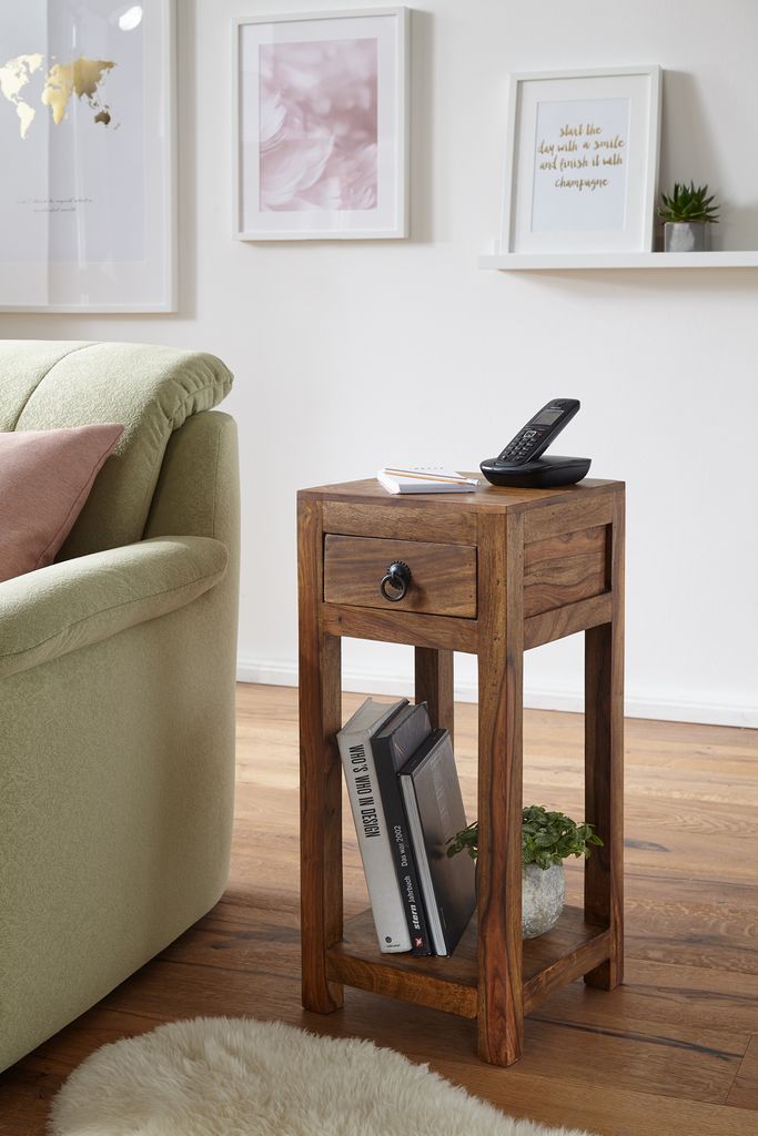 A wooden side table with books and a phone sits next to a sofa in a living room.