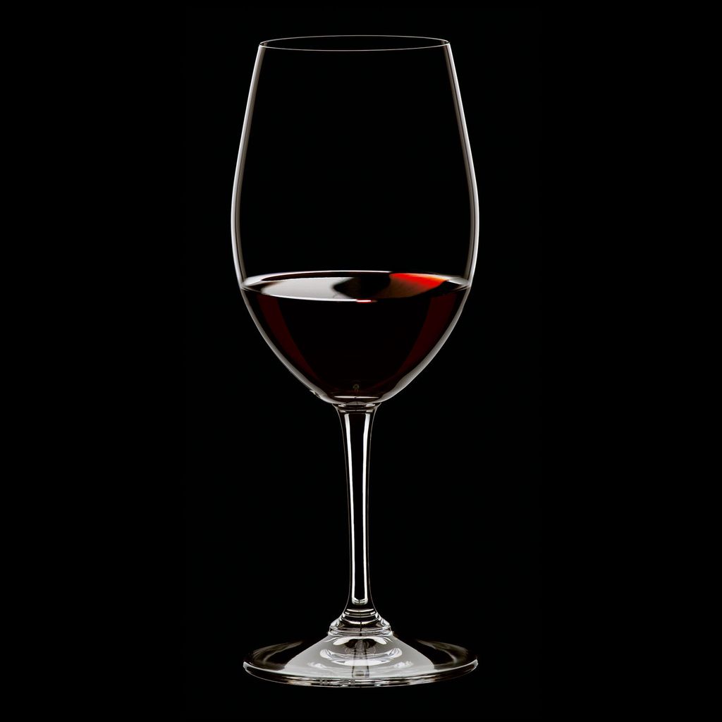 A single glass of red wine against a black background.