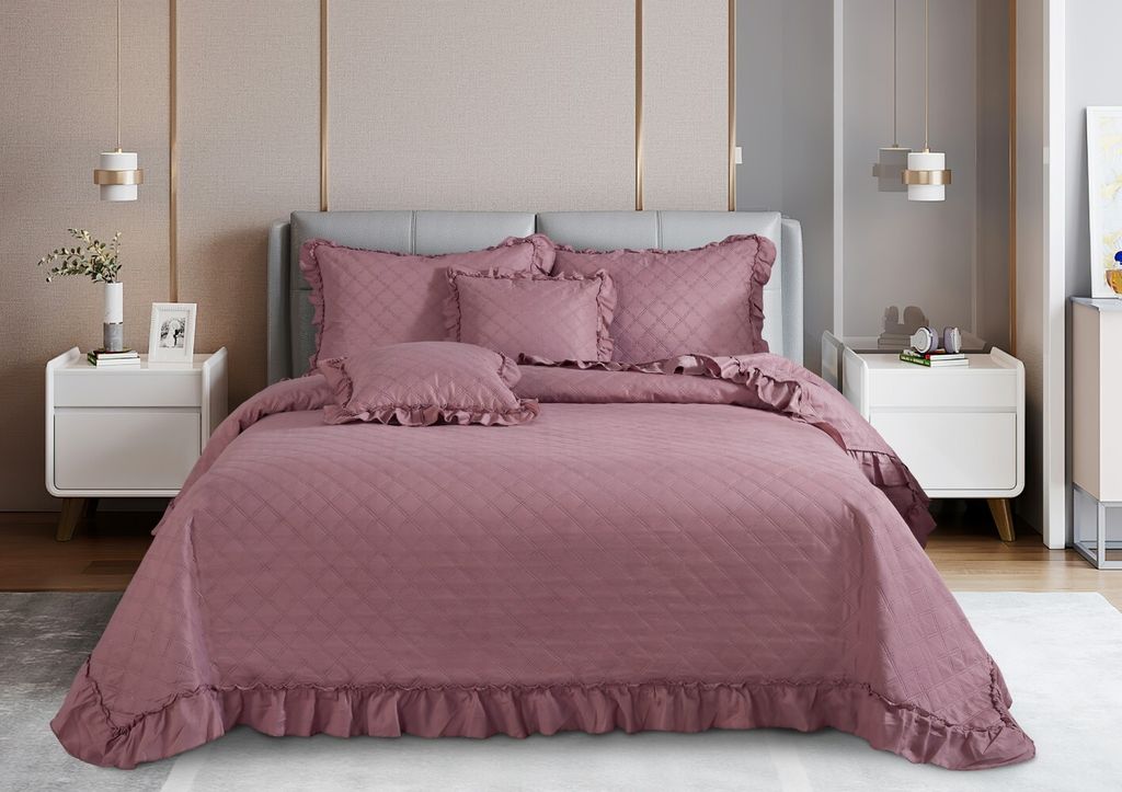 A bed with a pink quilted comforter and pillows in a bedroom setting.