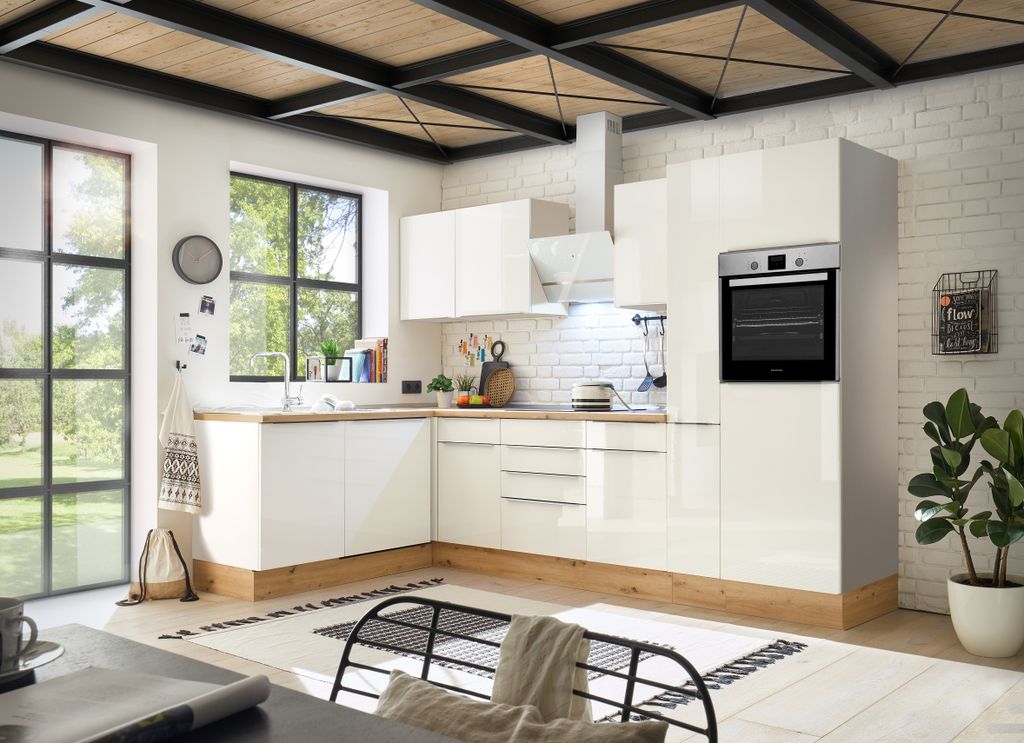 A modern, white L-shaped kitchen with wooden accents and a large window overlooking a garden.