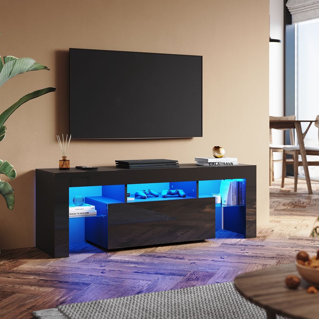 A modern living room with a black high-gloss TV stand featuring RGB lighting, a television, and decorative items.
