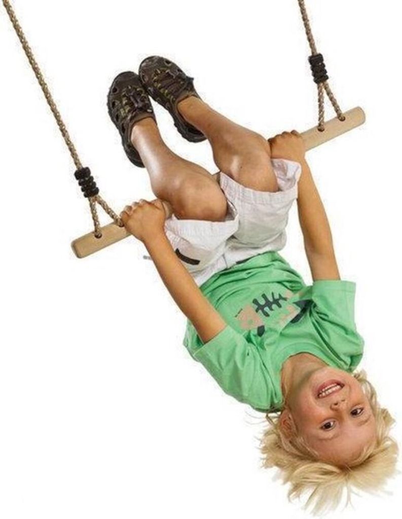 A young boy is upside down on a wooden trapeze swing.