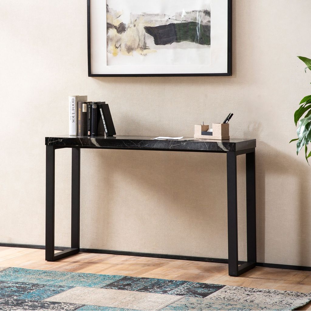 A console table with books and a pen holder on it, placed in a room with a painting on the wall and a rug on the floor.