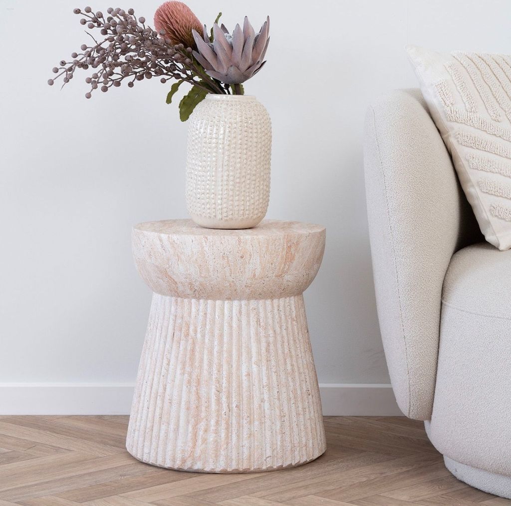 A decorative side table with a vase of flowers next to a sofa.