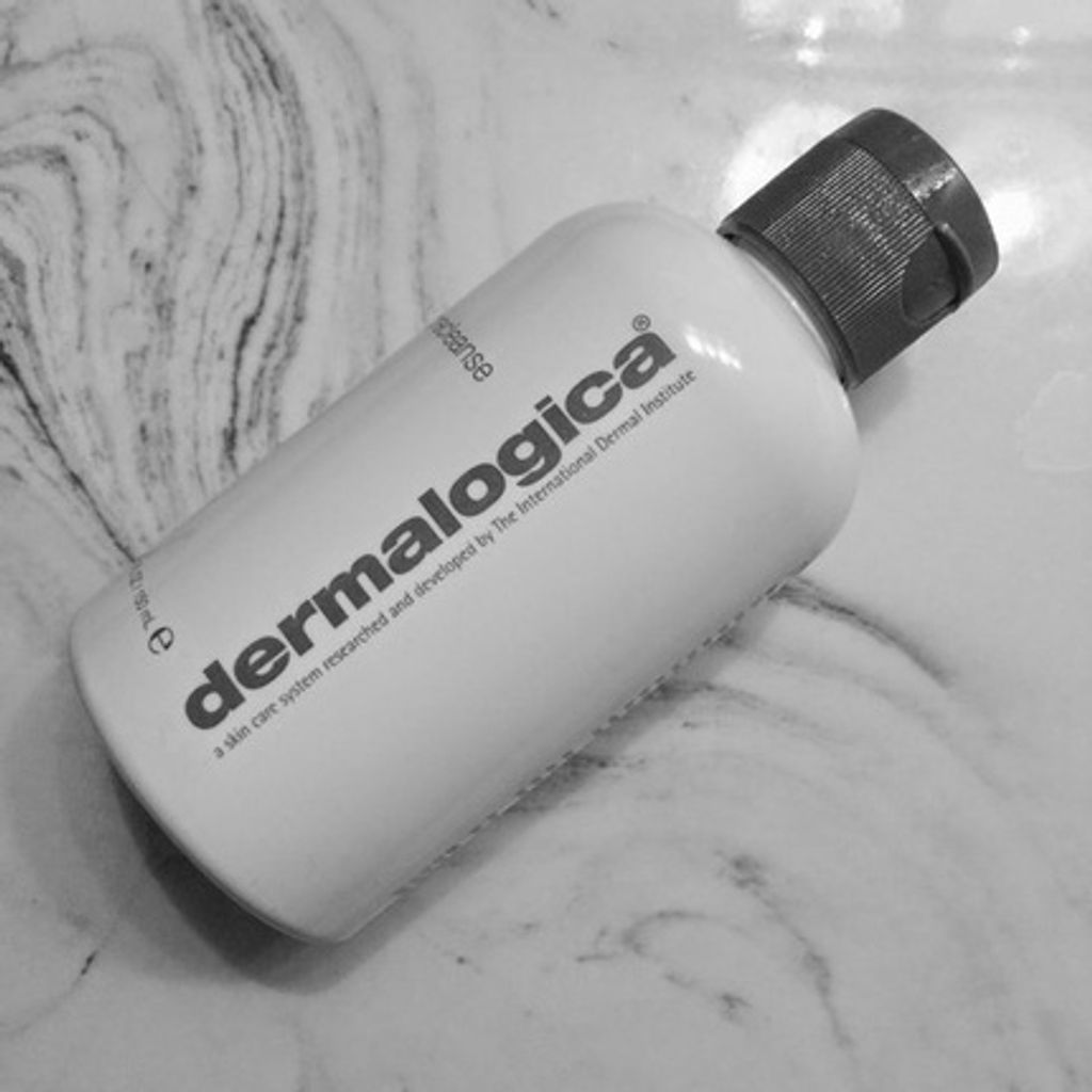 A white bottle of Dermalogica Precleanse is placed diagonally on a marble-like surface.