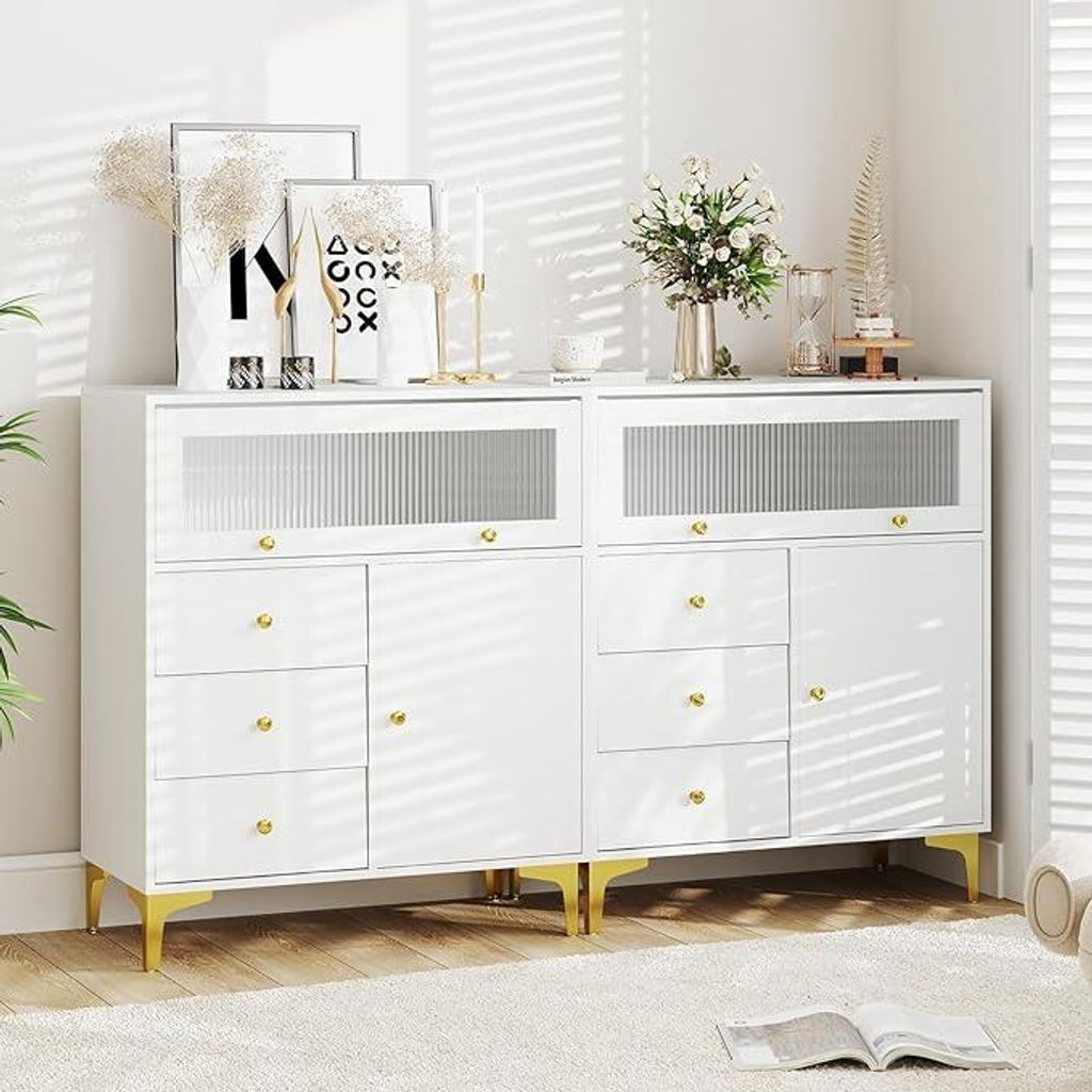 A white dresser with gold accents and decorative items on top, set against a white wall with blinds casting shadows.