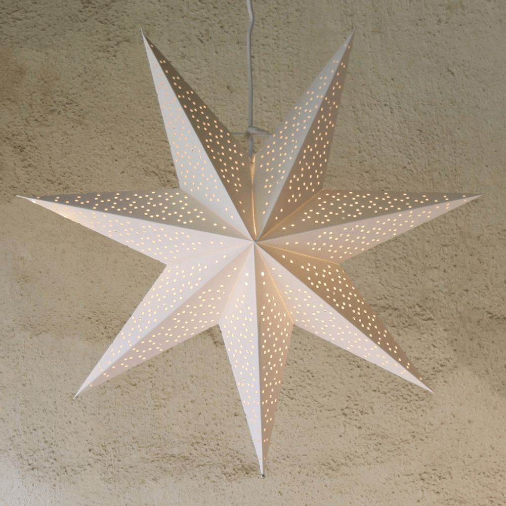 A white paper star lantern with many small perforations, hanging from a cord against a textured wall.