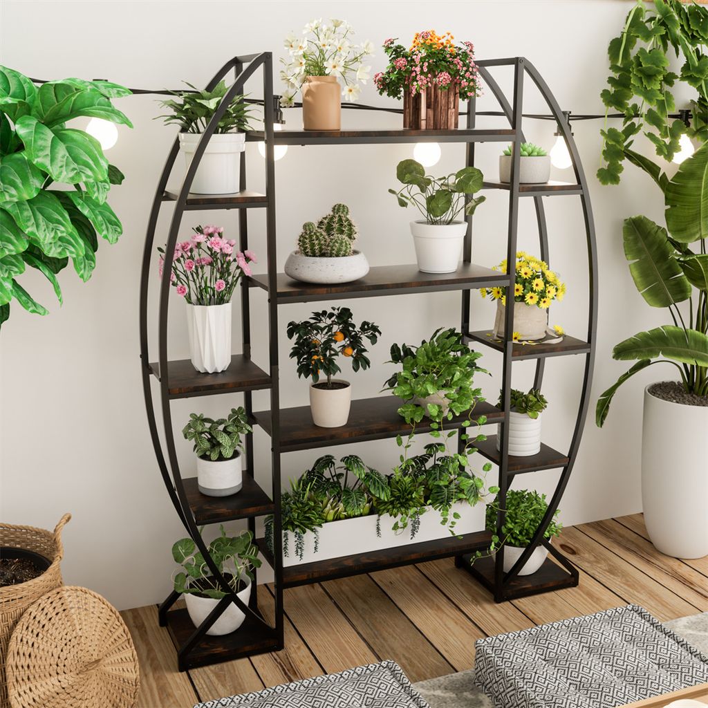 A circular metal plant stand filled with various potted plants, placed on a wooden floor indoors.