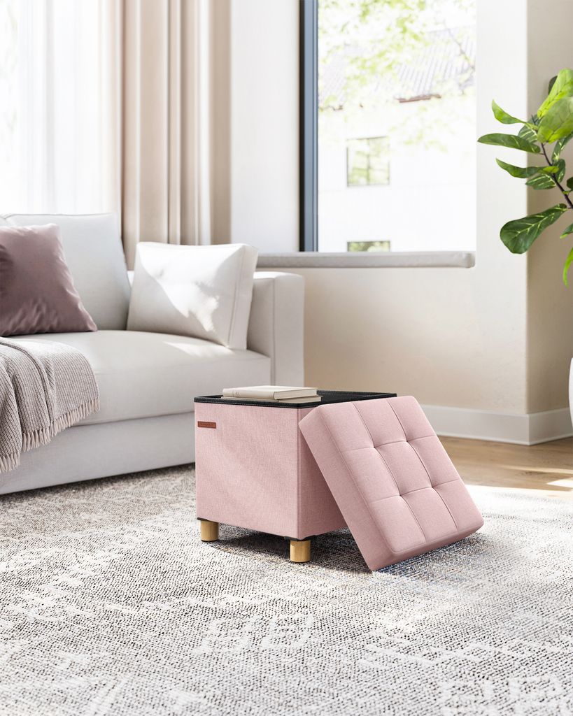 A pink ottoman with a lifted lid sits on a patterned rug next to a white sofa.