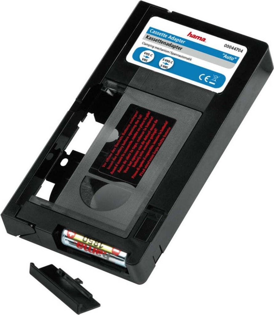 A Hama Videocassette Adapter for VHS-C to VHS conversion, shown from a slightly elevated angle against a white background. The adapter is black with a gray insert and a label with product information. Two batteries are visible in a compartment at the botto