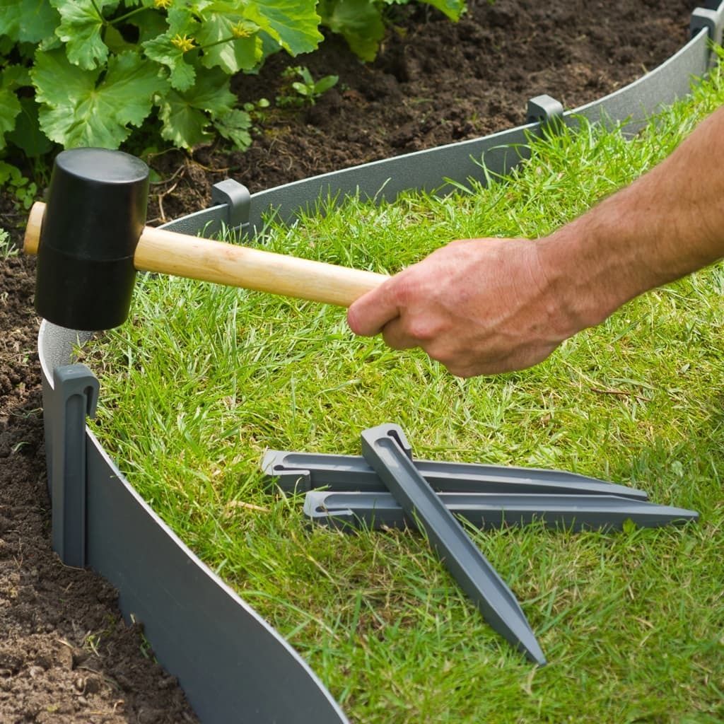 A person is using a mallet to hammer garden edging into the ground next to a plant.