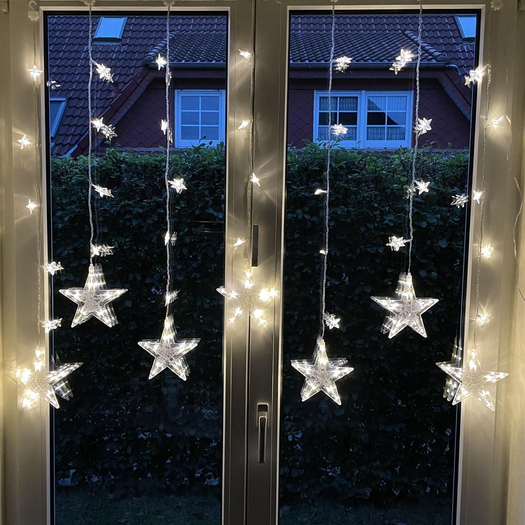 Star-shaped LED string lights hanging in a window at dusk.