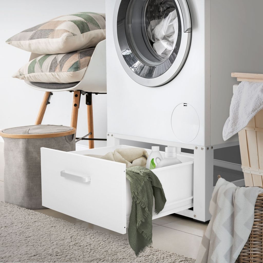 A laundry room scene with a washing machine, a drawer unit, a laundry basket, and pillows on a chair.
