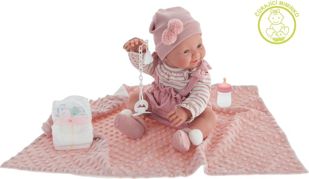 A baby doll is sitting on a pink blanket with a diaper and a baby bottle.