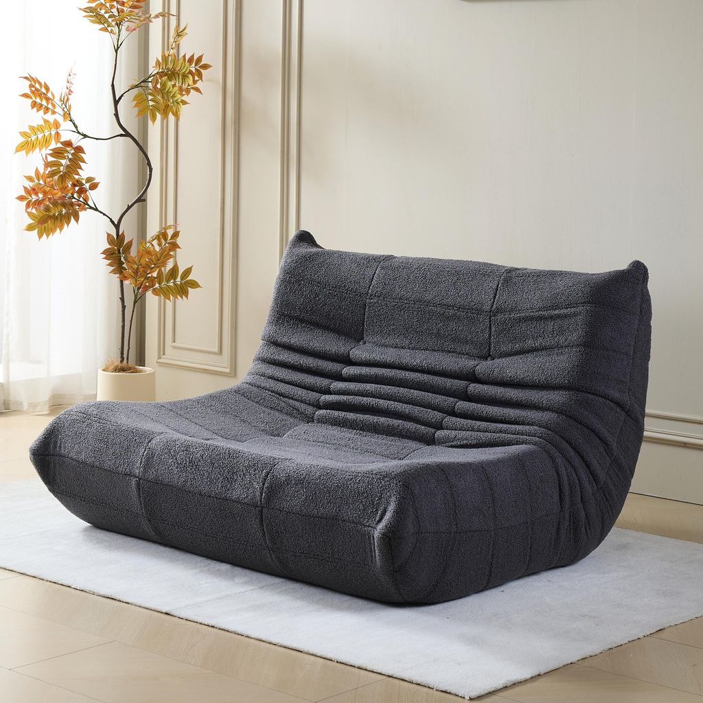 A dark gray sofa is placed on a light gray rug in a room with white walls and decorative molding.