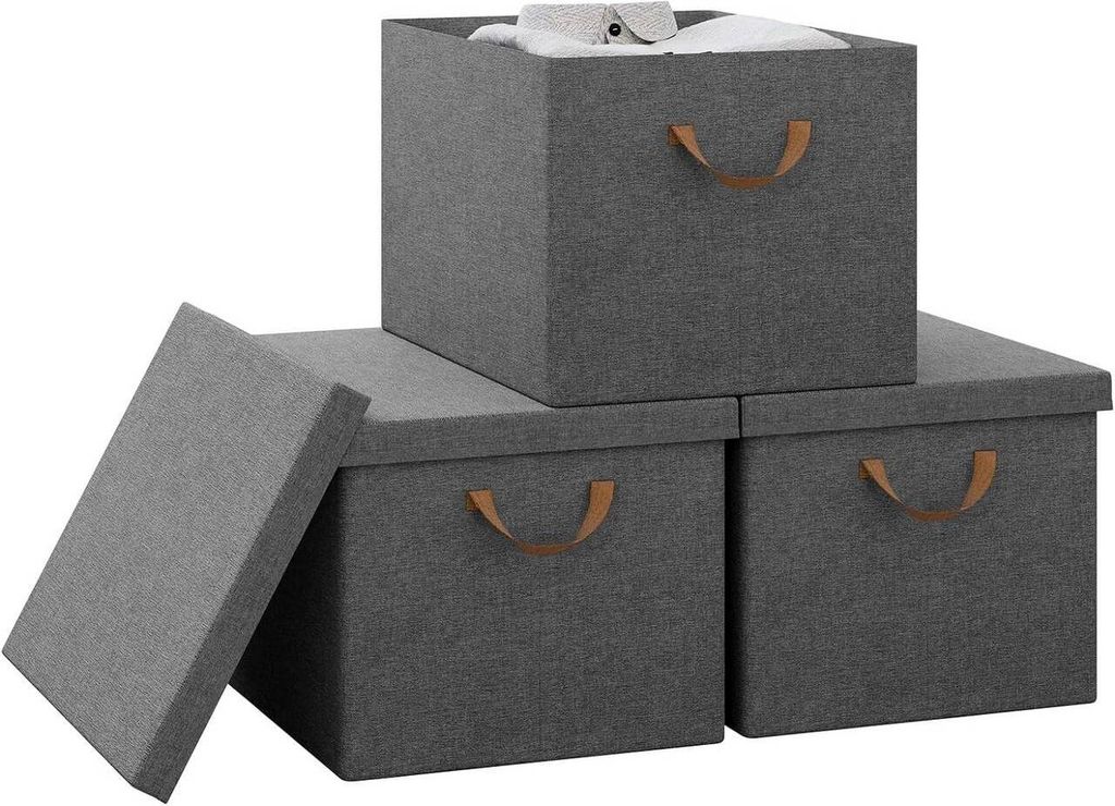 Three grey fabric storage boxes with brown handles are arranged on a white background. One box is stacked on top of two others, and its lid is propped open, revealing a white shirt inside. The lid of one of the bottom boxes is also open and leaning against