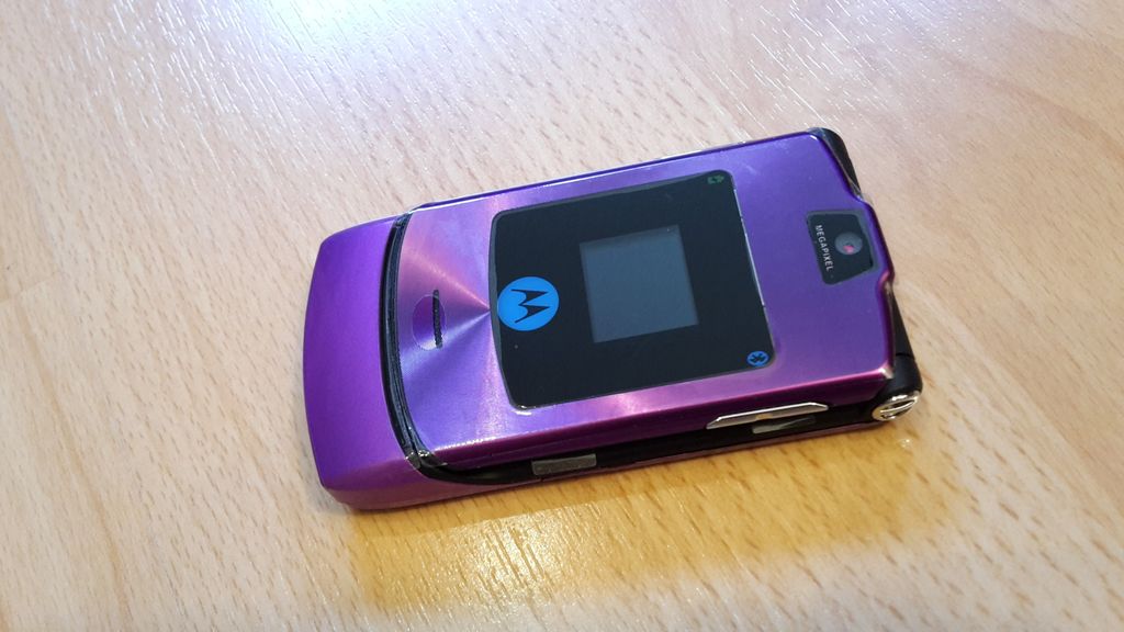 A purple Motorola RAZR V3i flip phone is lying on a wooden surface.