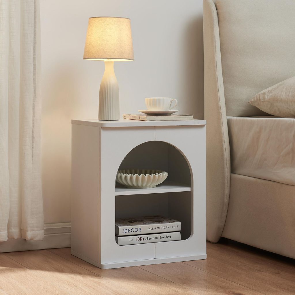 A white nightstand with two open shelves next to a bed.