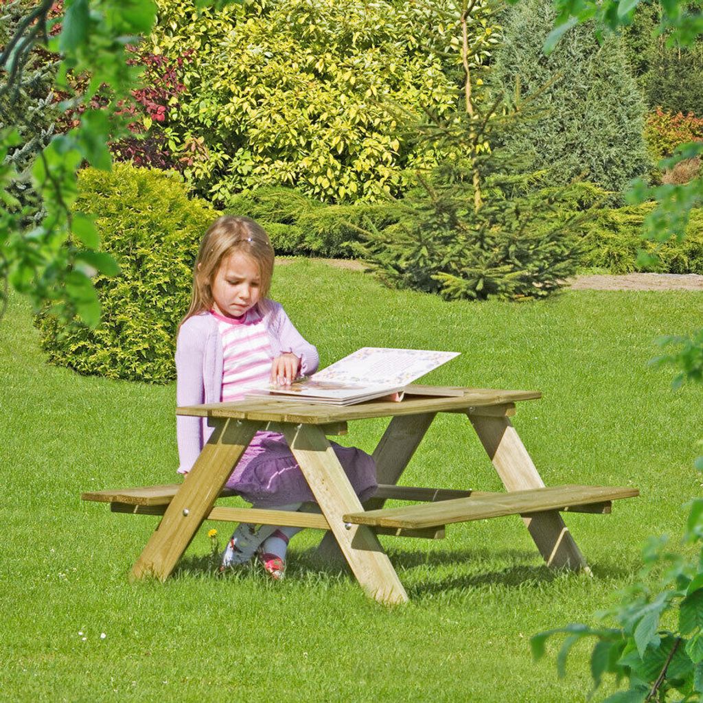 A young girl is sitting at a wooden picnic table in a garden, reading a book.