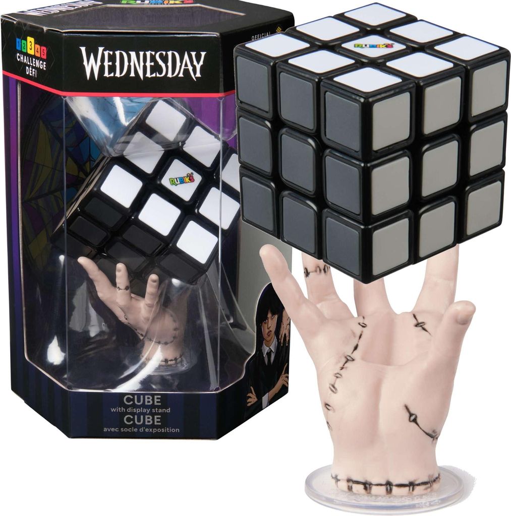 A Wednesday-themed Rubik's Cube is displayed in its packaging, with a hand-shaped display stand.