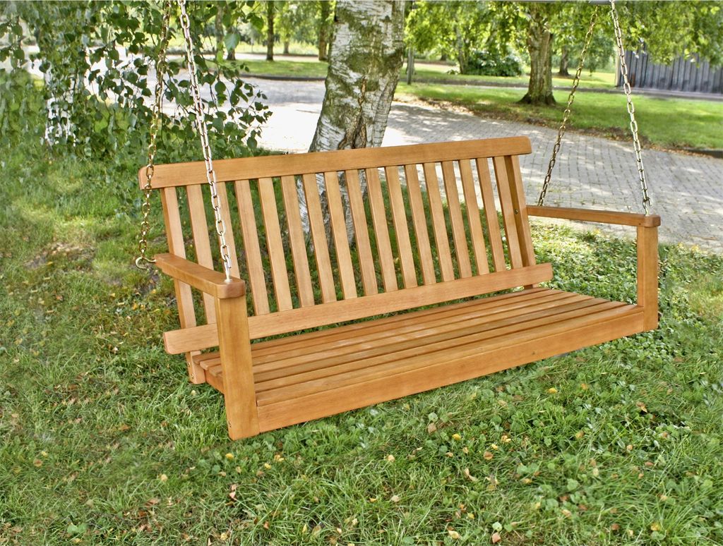 A wooden swing bench is hanging from a tree in a garden setting.