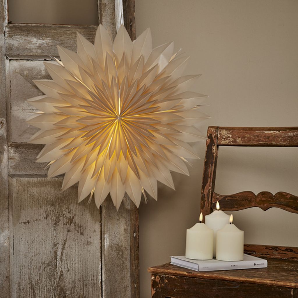 A paper star lantern is displayed on a rustic wooden door, with three white pillar candles on a wooden chair in the foreground.