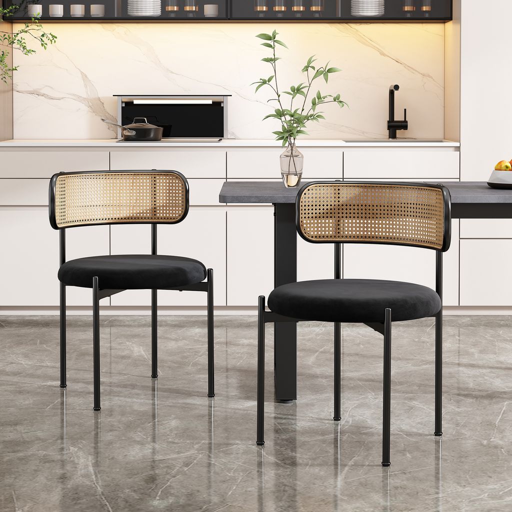 Two black velvet dining chairs with rattan backs are placed in a modern kitchen setting.