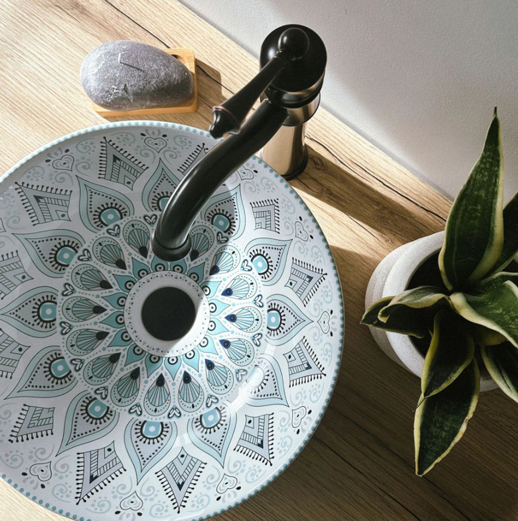 A decorative sink with a mandala pattern on a wooden countertop, next to a plant.