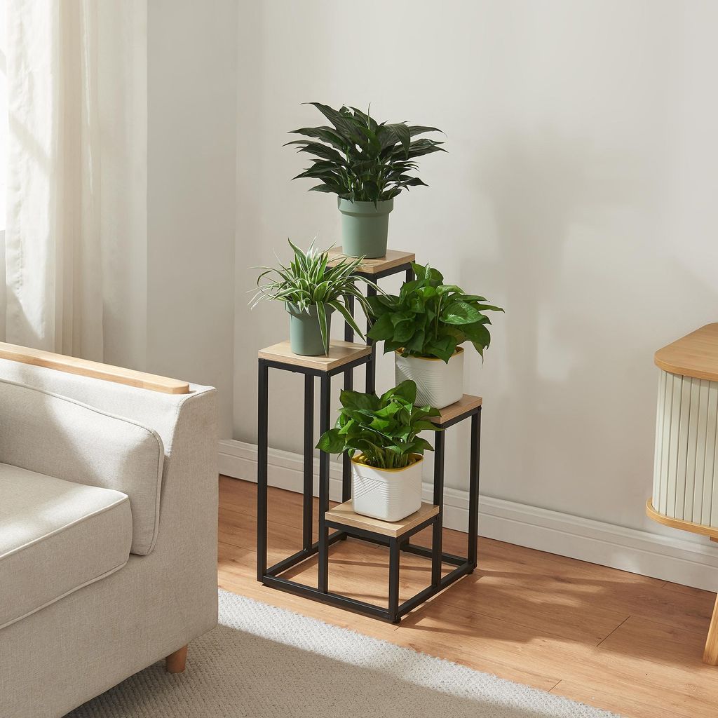 A plant stand with multiple plants is placed next to a sofa in a living room.