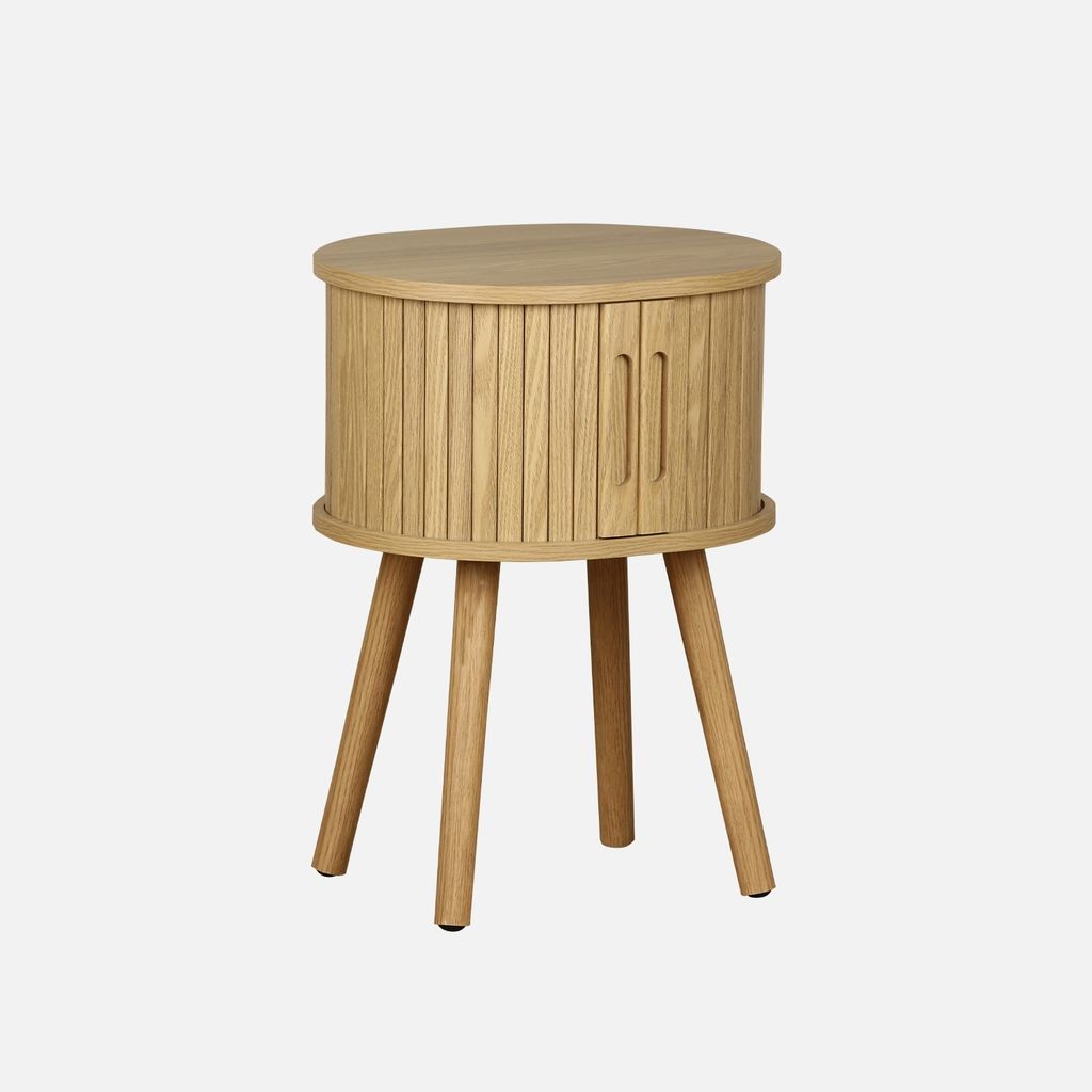 A round, wooden bedside table with a slatted cabinet and a single door, standing on three tapered legs. The table is shown against a plain white background.