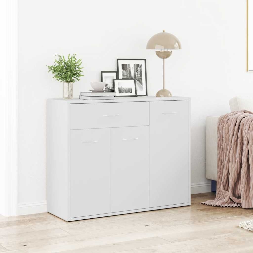 A white sideboard with drawers and doors, decorated with framed pictures, a plant, and a lamp.