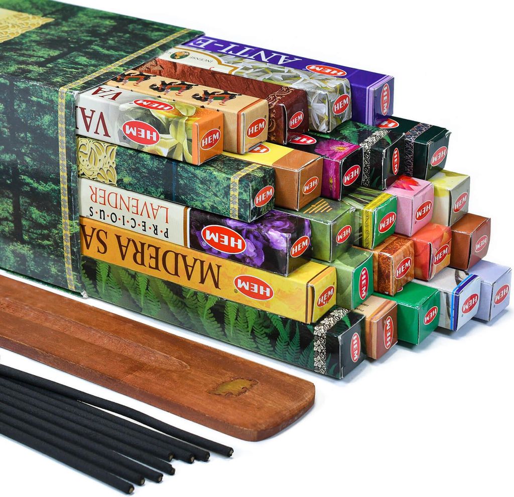 A collection of HEM incense boxes stacked in a pyramid shape, with a wooden incense holder and black incense sticks in the foreground.