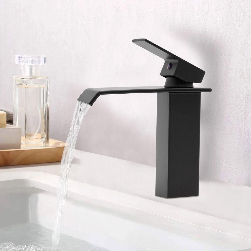 A black waterfall faucet in a bathroom sink with water flowing.