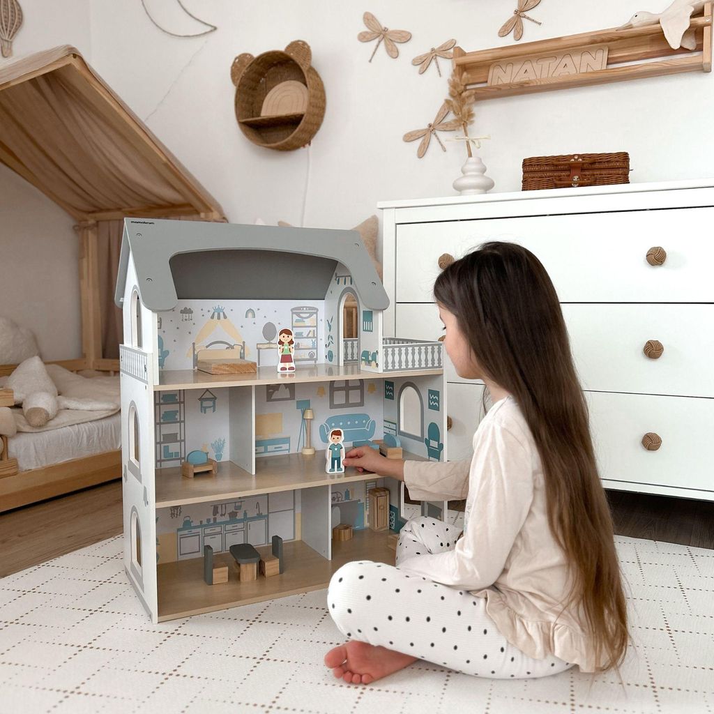 A young girl plays with a wooden dollhouse in a child's room.