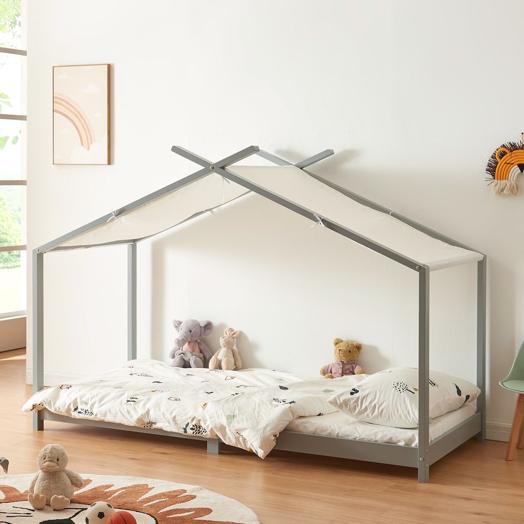 A child's bed with a house frame and canopy, decorated with stuffed animals and bedding, in a bedroom setting.