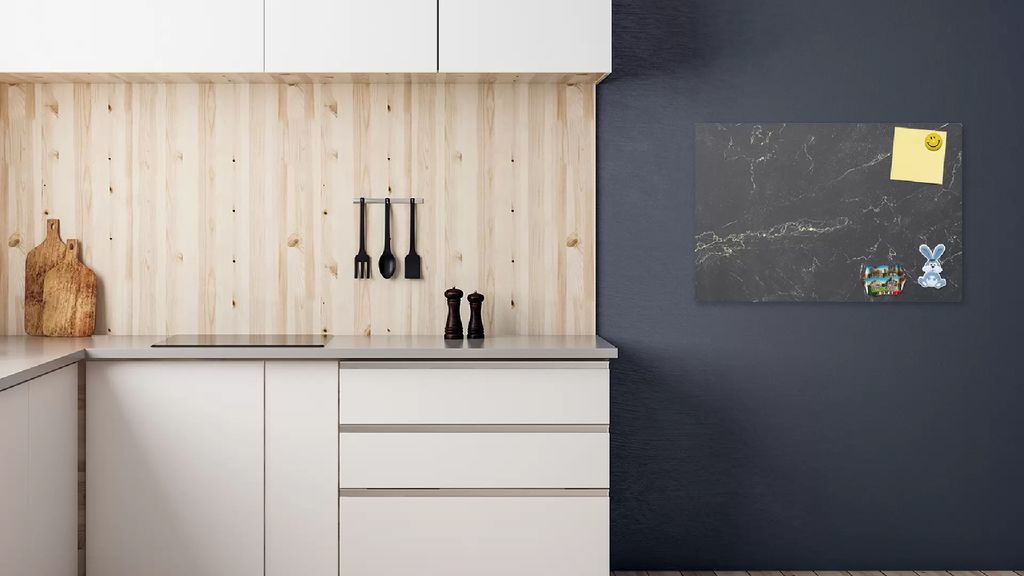 A modern kitchen with white cabinets and a wooden backsplash, featuring a black marble magnetic board on the dark gray wall.