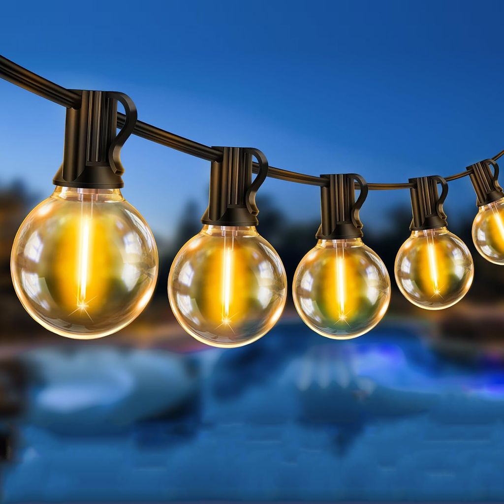 String lights with round bulbs hanging over a body of water at dusk.