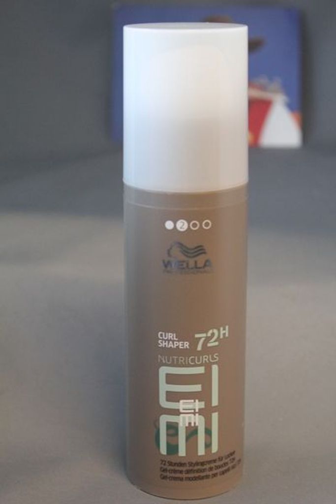 A bottle of Wella Professionals EIMI Nutricurls Curl Shaper is shown against a gray background.