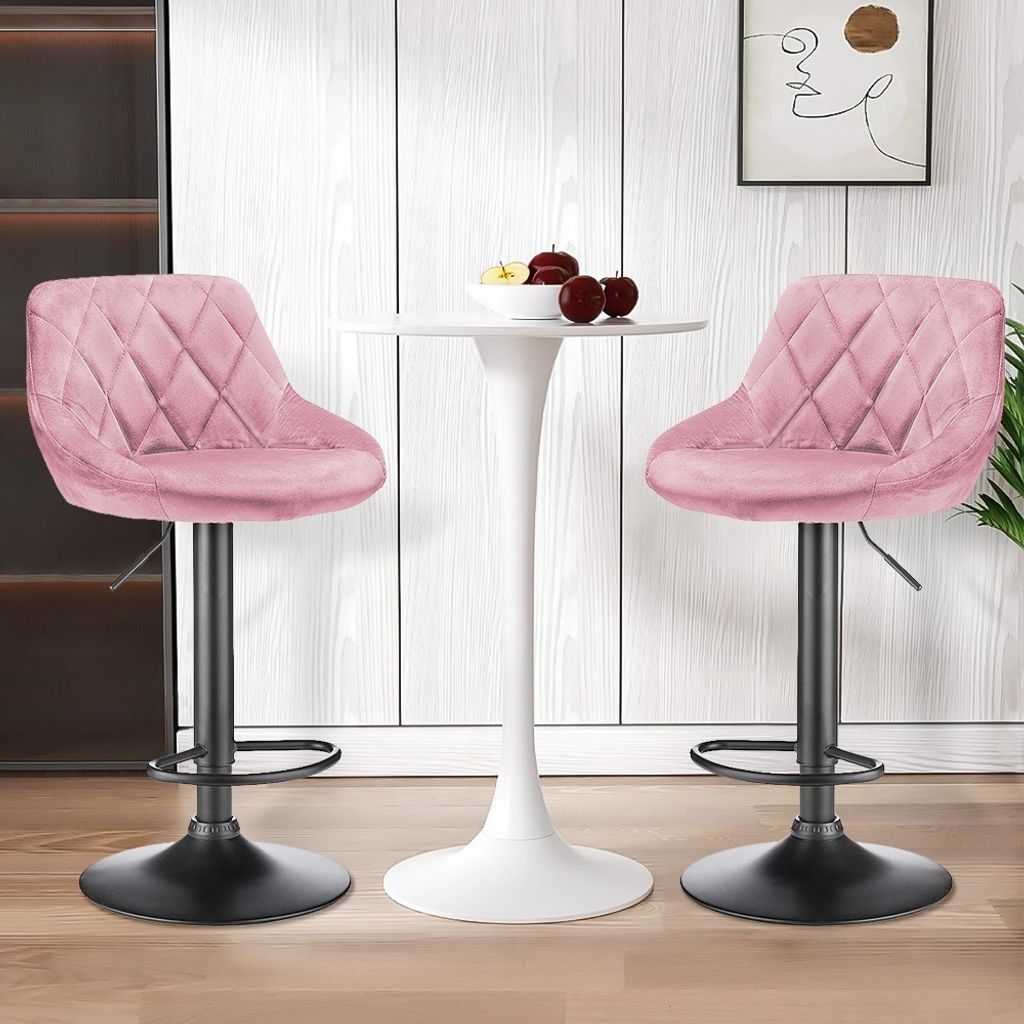 Two pink velvet bar stools are placed around a white tulip-style table, with a framed abstract artwork on the wall behind.