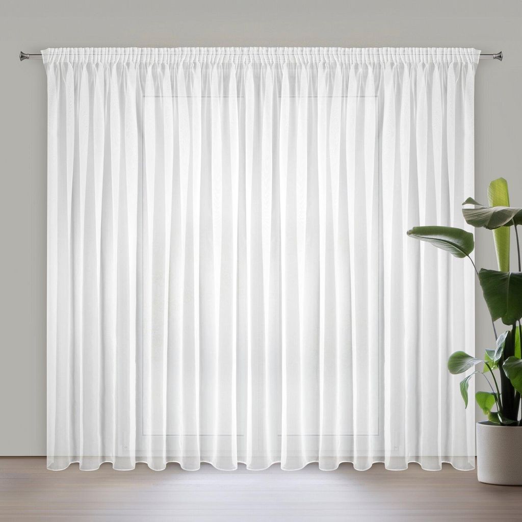 A white curtain hanging on a rod in front of a window, with a potted plant to the right.