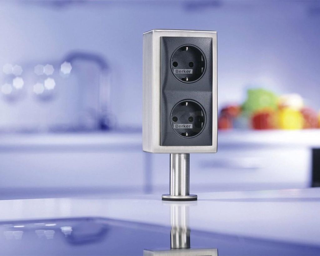 A stainless steel power outlet with two sockets, mounted on a countertop in a modern kitchen.