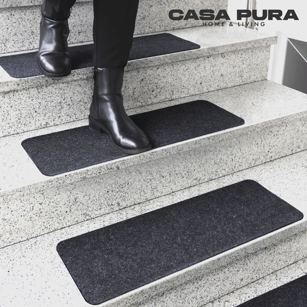 A person wearing black boots walks down a set of stairs with dark gray stair mats.