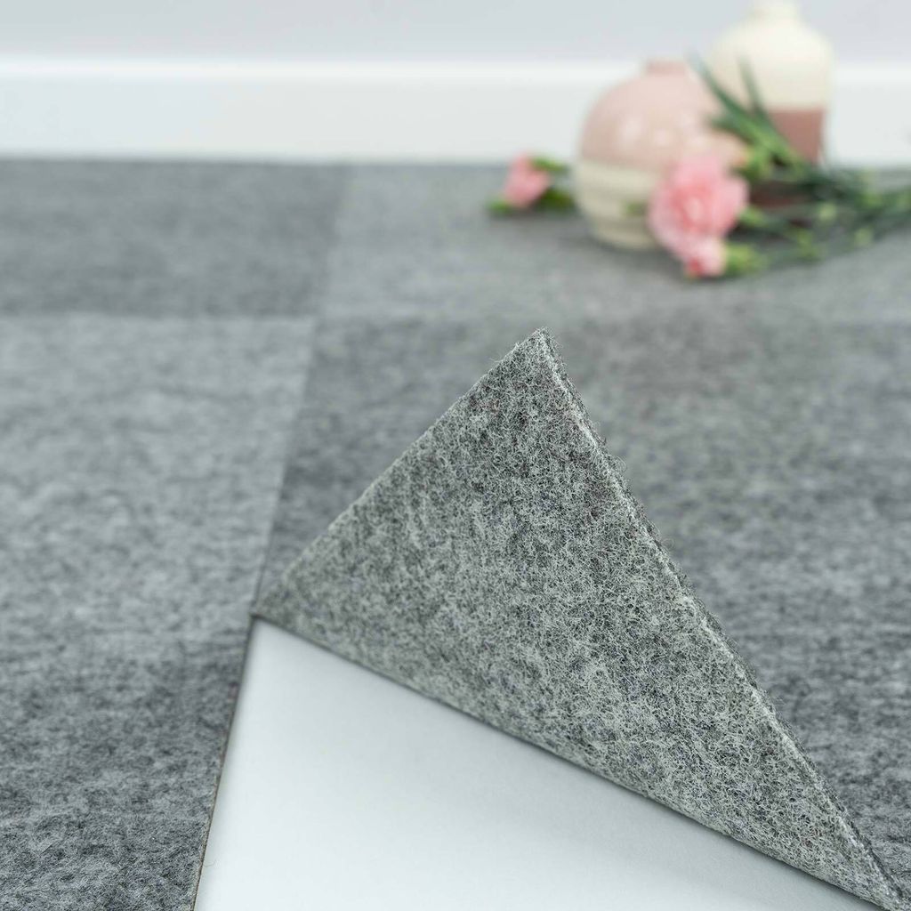 A close-up of grey carpet tiles, with one tile lifted to show the adhesive backing.