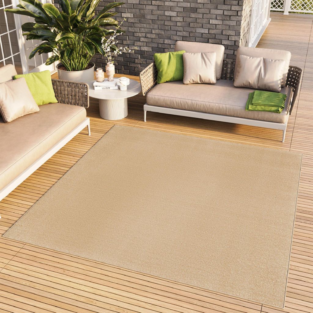 An outdoor living space with a sofa, chairs, a coffee table, and a large rug on a wooden deck.