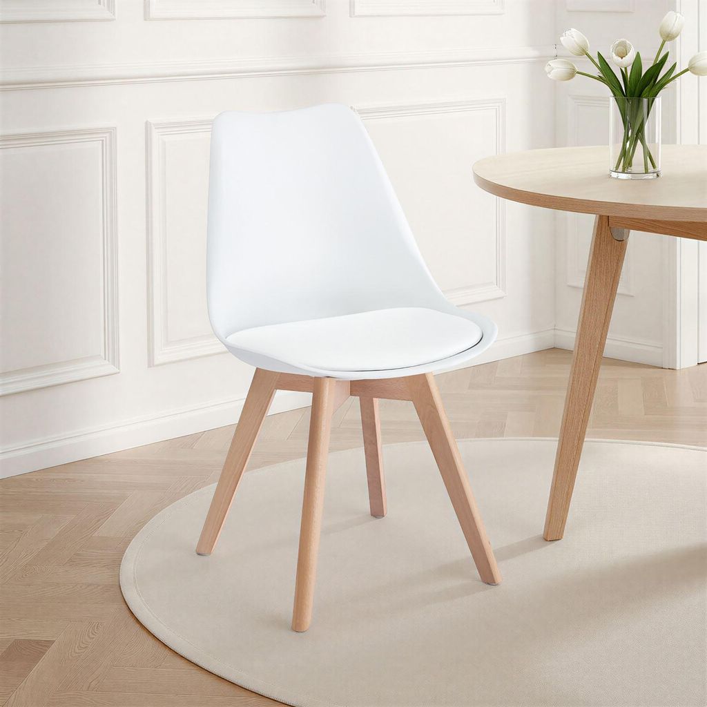 A white dining chair with wooden legs is placed on a light-colored rug in front of a white paneled wall.