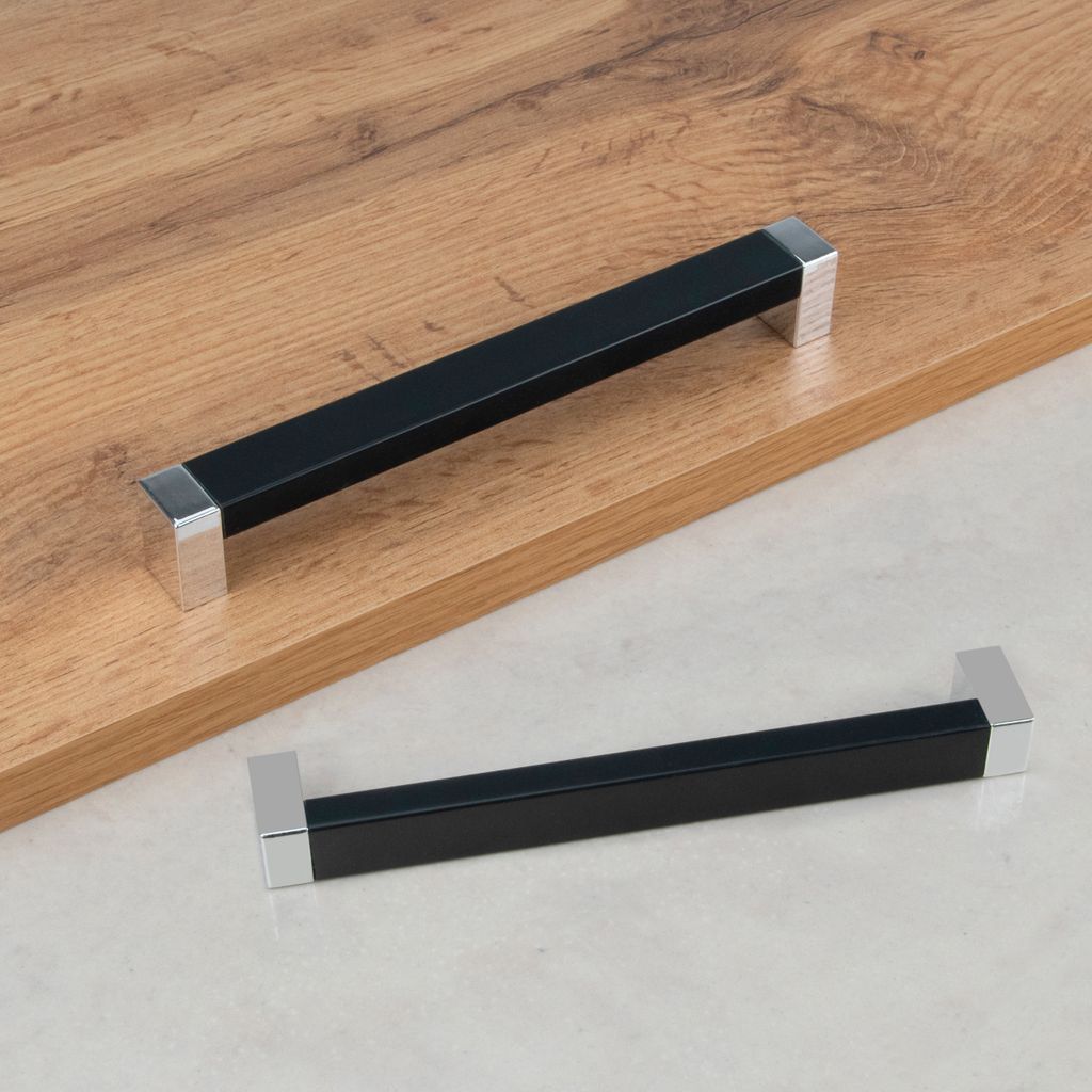Two modern black and silver cabinet handles are displayed on a light wood surface and a light gray surface.