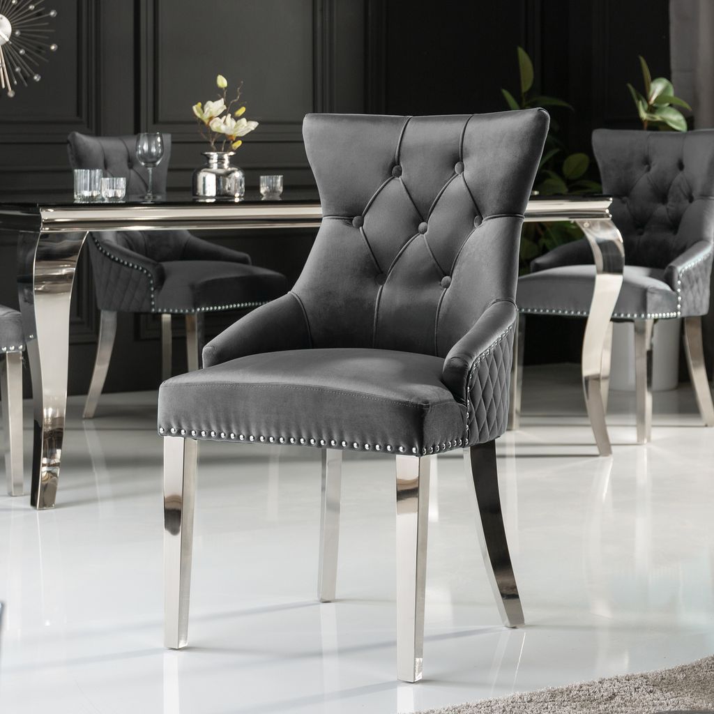 A grey velvet dining chair with silver legs and studding, placed in a dining room setting.
