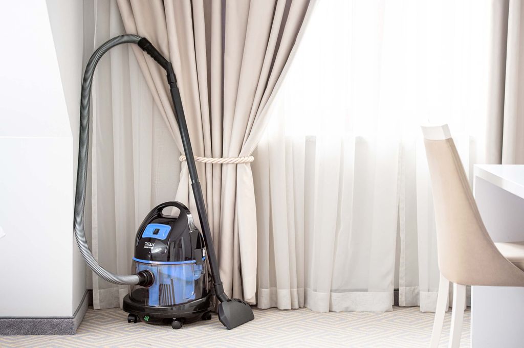 A vacuum cleaner is placed in a corner next to a window with curtains.