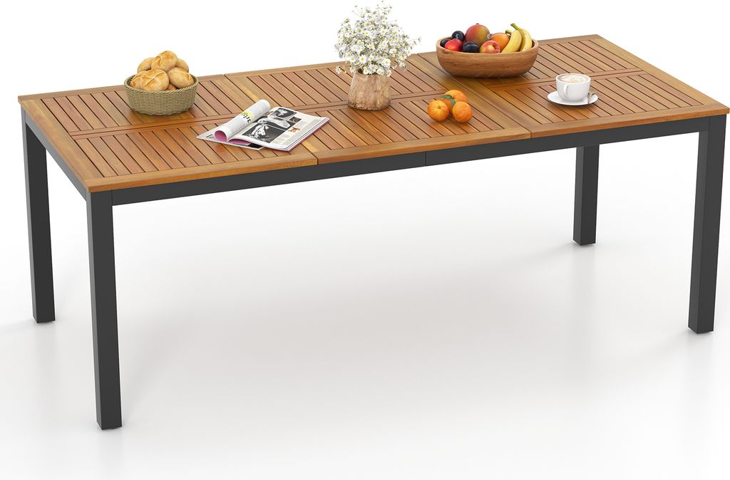 A wooden slatted table with a black metal frame, set with a bowl of fruit, a cup of coffee, a magazine, and a basket of bread rolls.